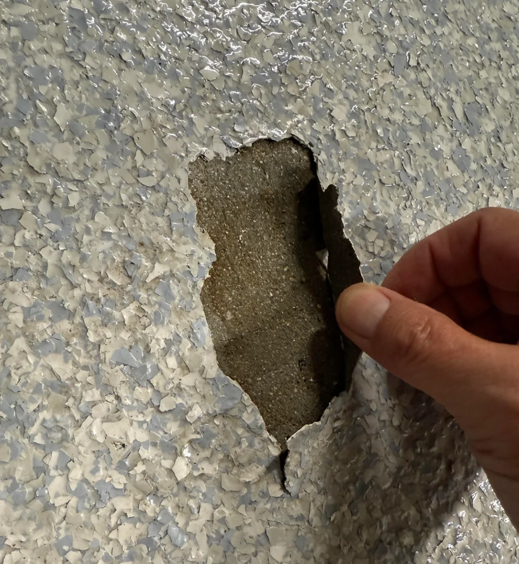 A photo of a spot where the epoxy is peeling. Homeowner is pulling back cracked area of the epoxy